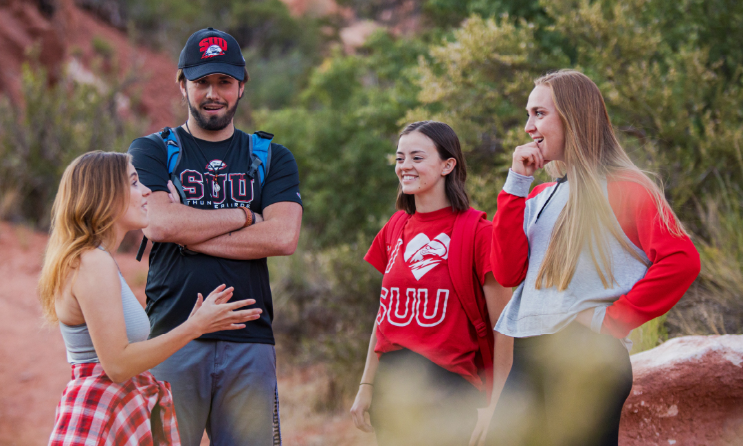 Students talking in nature, with pops of red clothing.